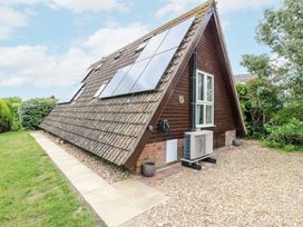 An A-frame house with solar panels on the roof a paved walkway grassy area and gravel driveway at Kingfisher in Isleham