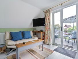 A living room with a sofa, coffee table, wall-mounted TV, floral curtains, and glass doors opening to an outdoor balcony at Kingfisher in Isleham