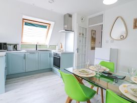 A kitchen with blue cabinets green chairs glass dining table and a window at Kingfisher in Isleham