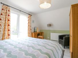 A bedroom with a bed and patterned curtains next to a window a wooden desk with a chair a wardrobe a black armchair and a floor lamp at Kingfisher in Isleham
