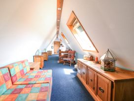 A narrow attic room with a colorful sofa, wooden cabinets, chair, bed, and skylight windows at Kingfisher in Isleham
