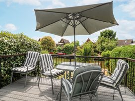 An outdoor deck with a table an umbrella and four cushioned chairs overlooking greenery and houses at Kingfisher in Isleham