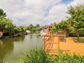 A wooden deck with chairs by a river with boats and houses along the riverbank at Kingfisher in Isleham