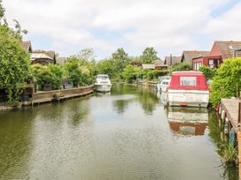 A canal with boats docked along both sides and houses with gardens along the banks at Kingfisher in Isleham
