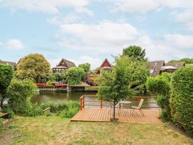 A backyard with a wooden deck overlooking a river with houses on the opposite bank at Kingfisher in Isleham