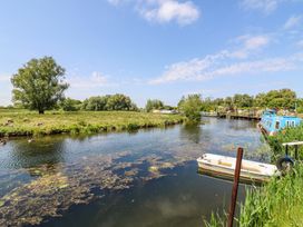 A river with boats docked along the bank and sheep grazing on grass in the field at Kingfisher in Isleham