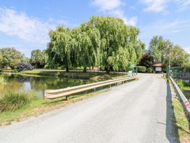 A road with guardrails crossing over water next to large trees and greenery at Kingfisher in Isleham