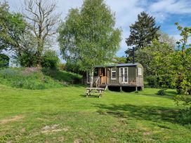 A small house with a wooden porch surrounded by trees and grass with a picnic table on the lawn at Mucklewick Hollow in Minsterley near Bishops Castle