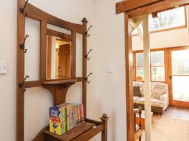 A wooden hall stand with coat hooks and a Roald Dahl book collection on a shelf next to a doorway leading to a sitting area with floral sofa at The Apple House in Spaxton near Nether Stowey