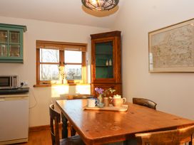 A kitchen with a wooden dining table and chairs a corner cabinet window and microwave at The Apple House in Spaxton near Nether Stowey