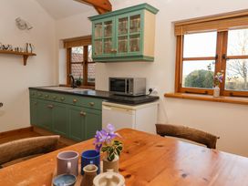 A kitchen with green cabinets wooden table and chairs with a microwave and vases near windows at The Apple House in Spaxton near Nether Stowey