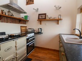 A kitchen with a stove toaster kettle sink shelves and wooden floor at The Apple House in Spaxton near Nether Stowey