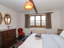 A bedroom with a bed a wooden chest of drawers two mirrors a red chair and windows with curtains at The Apple House in Spaxton near Nether Stowey