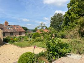 A garden with shrubs, flowers, lawn, and a house with a tiled roof at The Apple House in Spaxton near Nether Stowey