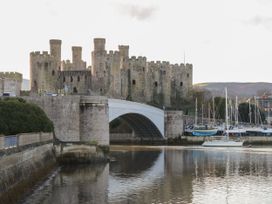 A stone castle with a bridge over a river and boats docked near the castle at The Old Coach House in Conwy