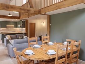 A dining area with a wooden table set with plates and glasses next to a living area with gray sofas and a kitchen with green cabinets at Swallows Lodge in Dormansland