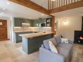 An open kitchen with green cabinets and wooden countertop next to a gray sofa and a fireplace at Swallows Lodge in Dormansland