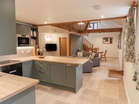 An open plan kitchen and living area with wooden beams a dining table and a gray sofa at Swallows Lodge in Dormansland
