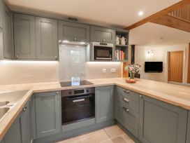 A kitchen with green cabinets wooden countertops built-in oven and microwave open shelving with teapots and books at Swallows Lodge in Dormansland