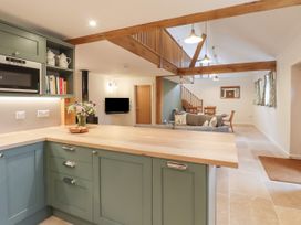 An open-plan kitchen and living area with wooden beams a table and chairs and a mounted television at Swallows Lodge in Dormansland