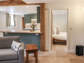 A living area with a grey sofa and wooden stool next to a kitchen with green cabinets and a bedroom with a white bed at Swallows Lodge in Dormansland