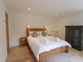 A bedroom with a wooden bed, white bedding, two patterned pillows, folded towels, wooden bedside tables, a black decorative wardrobe, and stone tile flooring at Swallows Lodge in Dormansland