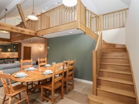 A dining area with a wooden table and chairs next to a wooden staircase and a mezzanine level at Swallows Lodge in Dormansland