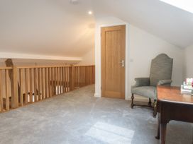 A hallway with a wooden railing a wooden door a grey armchair and a wooden table with books and flowers at Swallows Lodge in Dormansland