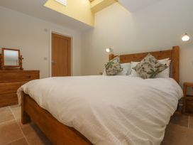 A bedroom with a wooden bed, white bedding, two leaf-patterned pillows, a wooden dresser with a mirror and a wooden door at Swallows Lodge in Dormansland