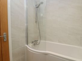 A bathroom with a white bathtub and a mounted shower head at Swallows Lodge in Dormansland