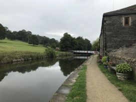 A view of a canal path alongside water with trees and a bridge at Millside View in Kildwick