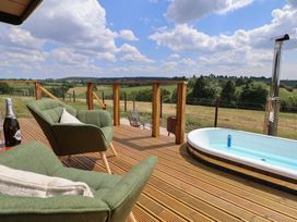 A wooden deck with two green armchairs a bottle a hot tub with water and a rural landscape at The Coop in Aston near Woore