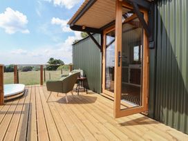 A wooden deck with a green chair small table and glass door at The Coop in Aston near Woore