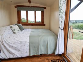 A bedroom with a bed covered in patterned bedding and pillows next to a window and a glass door leading to an outdoor deck at The Coop in Aston near Woore