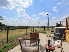 An outdoor patio with two chairs a small table with champagne glasses and bottle a fire pit hot tub and a grassy field at The Coop in Aston near Woore