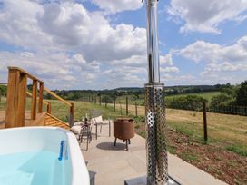 An outdoor patio with a hot tub chairs a small table and a fire pit overlooking green fields at The Coop in Aston near Woore