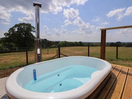 An outdoor hot tub on a wooden deck with a metal chimney and a field in the background at The Coop in Aston near Woore