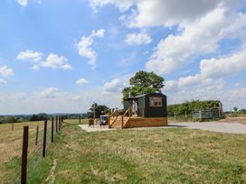 A small cabin on a wooden platform with a fenced grassy field under a blue sky at The Coop in Aston near Woore