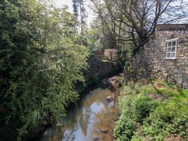 A narrow stream bordered by stone walls and green trees with a stone building on the right side at The Green in Lastingham
