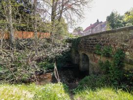 A stone bridge over a stream with trees and grass nearby and houses in the background at The Green in Lastingham