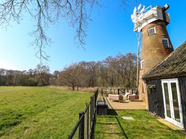 An outdoor deck with seating next to a windmill and grassy field at Wayford Mill in Wayford