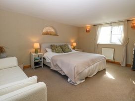 A bedroom with a double bed two bedside tables with lamps a window with curtains and a white sofa at Wayford Mill in Wayford