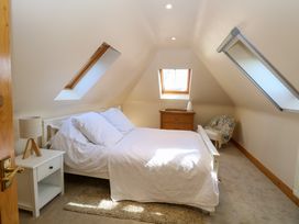 A bedroom with a white bed and pillows two skylight windows a bedside table with a lamp a wooden chest of drawers and a chair with a blanket at Wayford Mill in Wayford