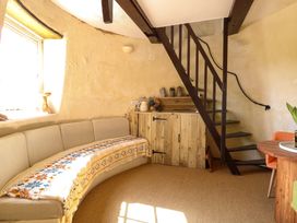 A small living area with a curved sofa covered by a patterned blanket a wooden cabinet under stairs and a round wooden table with an orange chair at Wayford Mill in Wayford