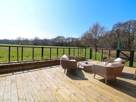 An outdoor wooden deck with three wicker chairs and a glass table overlooking a grassy field and trees at Wayford Mill in Wayford