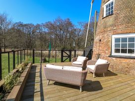 An outdoor deck with wicker chairs and a sofa near a brick building with a window and trees in the background at Wayford Mill in Wayford