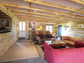 A living room with three sofas a wooden coffee table a bar counter with stools and wooden walls at Wayford Mill in Wayford