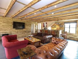 A sitting area with red and brown leather sofas a wooden coffee table a wall-mounted television and a wooden bar with chairs at Wayford Mill in Wayford