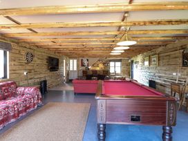 A room with a pool table red sofas a dart board and a television mounted on a wooden wall at Wayford Mill in Wayford