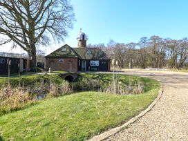 A brick house with a tiled roof and a small pond with reeds in front at Wayford Mill in Wayford